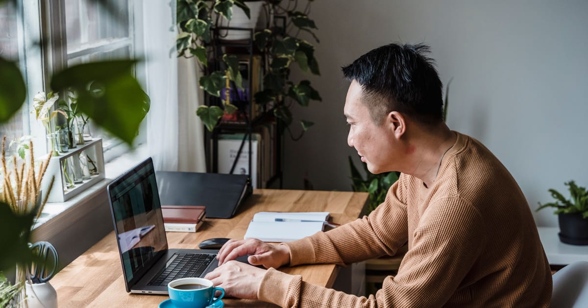 一名亞洲男士穿著便服，獨自在家中木桌前用手提電腦工作